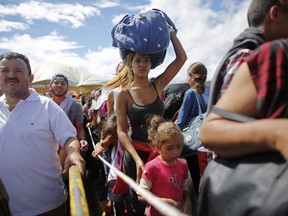 FILE - In this July 17, 2016 file photo, a woman carrying a bundle on her head waits in line to cross the border into Colombia through the Simon Bolivar International Bridge in San Antonio del Tachira, Venezuela. An estimated 25,000 Venezuelans trek across the international bridge into Colombia each day. Many come for a few hours to work or trade goods on the black market. But increasingly, they are coming to eat in one of a half-dozen facilities offering the increasingly hungry Venezuelans a free plate of food. (AP Photo/Ariana Cubillos, File)