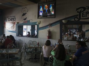 People sit in a coffee shop where the television carries a previously recorded video of Guatemala's President Jimmy Morales speaking to the nation in Guatemala City, Sunday, Aug. 27, 2017. Morales repeated in the video he was expelling the head of a U.N. anti-corruption commission that is investigating his campaign's financing, even after the nation's top court granted a temporary injunction blocking the order. (AP Photo/Moises Castillo)