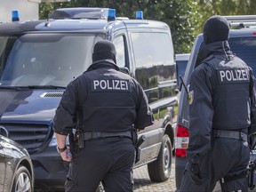 Police walk in front of a house in Banzkow, eastern Germany, Monday, Aug. 28, 2017. German prosecutors say authorities have raided the homes and workplaces of two people who apparently opposed the country's policy on migrants and are suspected of drawing up a "kill list" of left-wingers.  (Jens Buettner/dpa via AP)