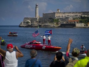 Lucas Oil SilverHook powerboat drivers Nigel Hook, waving a Stars and Stripes, and James Johnson, waving a Cuban national flag, stand aboard their speedboat, backdropped by "El Morro" castle, in Havana, Cuba, Thursday, Aug. 17, 2017. The team led by Hook, a California-based businessman, is claiming a record for a powerboat crossing from Florida to Cuba. The crew reports making it from Key West to Havana on Thursday in 1 hour and 18 minutes. (AP Photo/Ramon Espinosa)