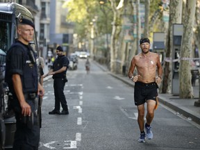 A man jogs by armed police officers standing next to their vans on a street in Las Ramblas, Barcelona, Spain, Friday, Aug. 18, 2017. Spanish police on Friday shot and killed five people carrying bomb belts who were connected to the Barcelona van attack that killed at least 13, as the manhunt intensified for the perpetrators of Europe's latest rampage claimed by the Islamic State group. (AP Photo/Manu Fernandez)