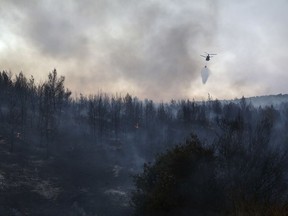 A helicopter drops its load over a forest fire at Kalamos village, north of Athens, on Sunday, Aug. 13, 2017.  Some dozens of wildfires broke out in Greece Saturday and more have done so Sunday, including on the beach resort of Kalamos near Athens. (AP Photo/Yorgos Karahalis)