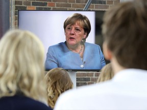 People watch from an adjoining room as German Chancellor Angela Merkel is interviewed by Youtubers and the online community in a livestream in Berlin, Germany, Wednesday, Aug. 16, 2017.  (Wolfgang Kumm/dpa via AP)