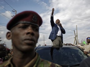 Kenya's President Uhuru Kenyatta, standing through the sunroof of the presidential vehicle, addresses his supporters as a presidential guard provides security, left, on a street in Ongata Rongai, on the outskirts of Nairobi, Kenya Tuesday, Sept. 5, 2017. Kenya faces an Oct. 17 vote after the Supreme Court nullified Kenyatta's re-election but opposition leader Raila Odinga said Tuesday he does not accept the date, demanding reforms to the electoral commission and other "legal and constitutional guarantees." (AP Photo/Ben Curtis)