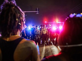 St. Louis County Police and Missouri State Highway Patrol troopers (C) stand guard as protesters (foreground) march on West Florissant Avenue in Ferguson, Mo., on August 9, 2015.