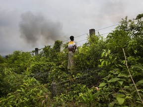 A Rohingya man stands near the barbed wire fence near the Bangladesh border town of Kutupalong town that marks the border with Myanmar and watches smoke rising from fires across the border in Myanmar, Monday, Sept. 4, 2017. (AP Photo/Bernat Armangue)