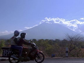 Motorists ride past by with Mount Agung volcano seen in the background in Karangasem, Bali, Indonesia, Thursday, Sept. 28, 2017. Warnings that the volcano on the tourist island will erupt have sparked an exodus as authorities have ordered the evacuation of villagers living within a high danger zone that in places extends 12 kilometers (7.5 miles) from its crater. (AP Photo/Firdia Lisnawati)
