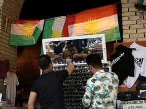 Men buy sunglasses from a street vendor underneath Kurdish flags in Irbil, 217 miles (350 kilometers) north of Baghdad, Iraq, Saturday, Sept. 23, 2017. Iraq's Kurdish region will vote on Monday's referendum for Kurdish independence, a vote dismissed as illegal and destabilising by the central government and the international community. (AP Photo/Khalid Mohammed)