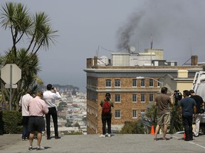 People stop to watch black smoke coming from the roof of the Consulate-General of Russia Friday, Sept. 1, 2017, in San Francisco. The San Francisco Fire Department says acrid, black smoke seen pouring from a chimney at the Russian consulate in San Francisco was apparently from a fire burning in a fireplace. The smoke was seen billowing from the consulate building a day after the Trump administration ordered its closure. (AP Photo/Eric Risberg)