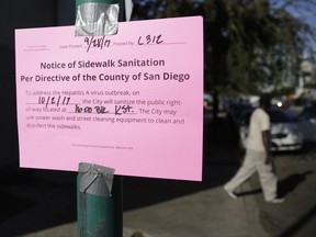 A man passes behind a sign warning of an upcoming street cleaning along 17th Street on Thursday, Sept. 28, 2017, in San Diego. The city of San Diego has cleared a downtown street where hundreds of homeless people regularly camp during ongoing efforts to sanitize neighborhoods to control the spread of hepatitis A. (AP Photo/Gregory Bull)