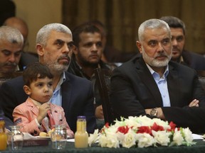 FILE - In this May 1, 2017, file photo, Gaza leader, Yehya Sinwar, left, holding his son Ibrahim, sits next to Ismail Haniyeh, right, a former top Hamas official in Gaza, as they listen to Khaled Mashaal, the outgoing Hamas leader in exile, during his news conference broadcast from Doha, Qatar, in Gaza City. The Islamic militant group Hamas has announced a number of key concessions to the rival Fatah movement, potentially paving the way for reconciliation after a 10-year rift that has left the Palestinians torn between two governments. (AP Photo/Adel Hana, File)