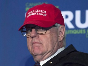 Former Industry minister and moderator John Manley puts on a red baseball cap as he jokes around before moderating a session with Innovation, Science and Economic Development Minister Navdeep Singh Bains at a conference in Ottawa, Wednesday October 12, 2016.