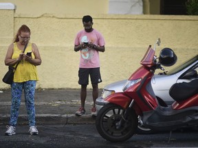 People stand at a wifi hotspot in the aftermath of Hurricane Maria with many cellphone towers downed in San Juan, Puerto Rico, Sunday, Sept. 24, 2017. (AP Photo/Carlos Giusti)