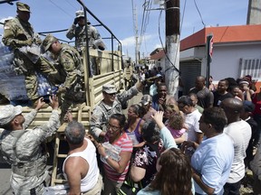 National Guardsmen arrive at Barrio Obrero in Santurce to distribute water and food among those affected by the passage of Hurricane Maria, in San Juan, Puerto Rico, Sunday, Sept. 24, 2017. Puerto Rico's nonvoting representative in the U.S. Congress said Sunday that Hurricane Maria's destruction has set the island back decades, even as authorities worked to assess the extent of the damage. (AP Photo/Carlos Giusti)