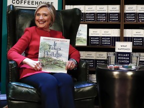 Hillary Clinton, holds her book "It Takes A Village" as she sits on stage at the Warner Theatre in Washington, Monday, Sept. 18, 2017, during a book tour event for her new book "What Happened" hosted by the Politics and Prose Bookstore. (AP Photo/Carolyn Kaster)