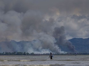 A Bangladeshi boy walks towards a parked boat as smoke rises from across the border in Myanmar, at Shah Porir Dwip, Bangladesh, Thursday, Sept. 14, 2017
