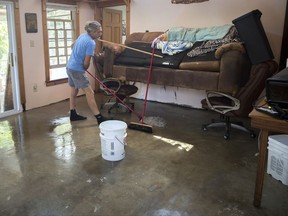 Gene Miles mops under his raised sofa, Tuesday, Sept., 12, 2017, while cleaning up from Tropical Storm Irma on Tybee Island, Ga. (AP Photo/Stephen B. Morton)