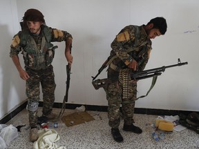 FILE - In this July 22, 2017 file photo, an Arab fighter, left, and Kurdish fighter, right, who fight together with the U.S.-backed Syrian Democratic Forces (SDF), hold their weapons as they prepare to move to the front line to battle against the Islamic State militants, in Raqqa, northeast Syria. U.S.-backed Syrian fighters are preparing to launch an offensive against the Islamic State group in eastern Syria along the border with Iraq in a race with government forces who are marching in the same direction in a crushing assault against the extremists in their last major holdout in Syria. (AP Photo/Hussein Malla, File)