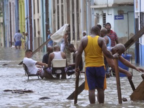 In this Sunday, Sept. 10, 2017 photo released by Granma, men play dominoes in the middle of a flooded street as others pull broken furniture from calf-high water in the aftermath Hurricane Irma, in Havana, Cuba. Eddy Dennis, a grey-haired 51-year-old parking attendant pulling furniture, said the scene was one of neighborly cooperation and mutual effort in the face of the city's worst flooding in years, if not decades. "It was something communal that all the neighbors were doing in the spirit of unity," Dennis said. "Those who got tired would sit down and play dominoes. We had spent the whole night on our feet and it was a way to destress in the face of disaster." (Juvenal Balan/Granma via AP)