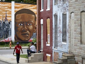 FILE - in this June 23, 2016 file photo, a mural depicting Freddie Gray is seen past blighted row homes in Baltimore, at the intersection where Gray was arrested. The U.S. Department of Justice won't bring federal charges against six police officers involved in the arrest and death of Freddie Gray, a young black man whose death touched off weeks of protests and unrest in Baltimore. The officers were charged by state prosecutors after Gray's neck was broken in the back of a police transport wagon in April of 2015. (AP Photo/Patrick Semansky File)