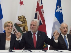 Quebec Premier Philippe Couillard, flanked by Ontario Premier Kathleen Wynne, left, and California Governor Edmund G. Brown, raise their hands after signing an agreement on climate change in Quebec City on Friday, Sept. 22, 2017. THE CANADIAN PRESS/Jacques Boissinot