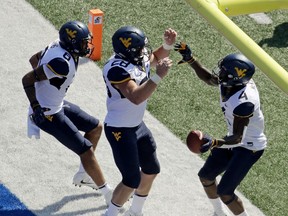 West Virginia running back Kennedy McKoy (4) celebrates with tight end Elijah Wellman (28) and wide receiver Marcus Simms (8) after scoring a touchdown during the first half of an NCAA college football game against Kansas Saturday, Sept. 23, 2017, in Lawrence, Kan. (AP Photo/Charlie Riedel)