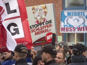 Protesters hold up posters that read "Stop human trafficker Merkel", and "Merkel must go!" during an election campaign event of Chancellor Angela Merkel's conservative Christian Union, CDU, in Wolgast, Germany on Sept. 8, 2017.