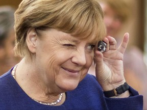 German Chancellor Angela Merkel peeks through the hole of a chicken god, which she got from a visitor during an election campaign in Vilmnitz, northern Germany, Saturday, Sept. 16, 2017. Chicken gods are finds with a natural hole and are considered as lucky charms. (Jens Buettner/dpa via AP)