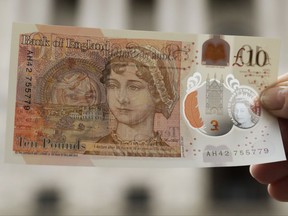 One of the new British 10 pound notes is posed for photographs outside the Bank of England in the City of London, Thursday, Sept. 14, 2017. The new polymer note, released for circulation on Thursday, features the renowned novelist Jane Austen and is the first UK banknote with a tactile feature to support blind and partially sighted users. (AP Photo/Matt Dunham)