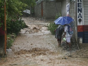 People walk under a downpour on a flooded street in Acapulco, Guerrero state, Mexico, Thursday, Sept. 14, 2017. Hurricane Max hit Mexico's southern Pacific coast as a Category 1 storm Thursday and was expected to move inland into Guerrero state, a region that includes the resort city of Acapulco.(AP Photo/Bernandino Hernandez)