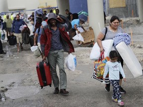 FILE - In this Sept. 9, 2017 file photo, evacuees are moved to another building with more bathrooms while sheltering at Florida International University ahead of Hurricane Irma in Miami.  Students in two of the nation's largest school districts still don't know when they'll return to class, forcing many Florida parents to juggle childcare as they head into a second week of recovering from Hurricane Irma. Miami-Dade and Broward counties had hoped to resume operations Monday, Sept. 18.. But dozens of schools in the two districts , which serve almost 700,000 students, are still without power. (AP Photo/David Goldman)