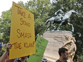 FILE - In this July 8, 2017, file photo, protesters carry signs in front of a statue of Confederate Gen. Thomas "Stonewall" Jackson as they demonstrate against a KKK rally in Justice Park in Charlottesville, Va. A resolution on removing the Jackson statue is on the Charlottesville City Council's agenda Tuesday night, Sept. 5, 2017. The city's decision earlier this year to remove a statue of Confederate Gen. Robert E. Lee helped spark a rally of white nationalists that descended into violence (AP Photo/Steve Helber, File)