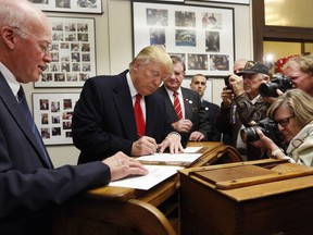 FILE - In this Nov. 4, 2015 photo, New Hampshire Secretary of State Bill Gardner watches, left, as Republican presidential candidate Donald Trump fills out his papers to be on the nation's earliest presidential primary ballot at The Secretary of State's office in Concord, N.H. Gardner said Friday, Sept. 8, 2017, that he will remain on the Presidential Advisory Commission on Election Integrity though he disagrees with voter fraud allegations made by the panel's vice chairman about his state.  (AP Photo/Jim Cole, File)