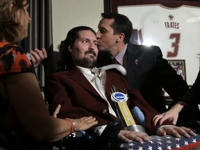 FILE - In this Dec. 13, 2016, file photo, former Boston College baseball captain Pete Frates, center left, receives a kiss from Boston College head baseball coach Mike Gambino after Frates was presented with the 2017 NCAA Inspiration Award, during ceremonies in Frates home in Beverly, Mass. The man who inspired the ice bucket challenge that has raised millions for ALS research is being honored at Boston City Hall. Mayor Martin Walsh is hosting a rally Tuesday, Sept. 5, 2017, for Frates at City Hall Plaza. The event coincides with the release of a new book on Frates. (AP Photo/Steven Senne, File)