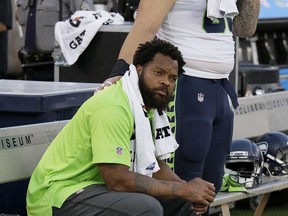 FILE - In this Aug. 31, 2017, file photo, Seattle Seahawks defensive end Michael Bennett sits during the playing of the national anthem before an NFL preseason football game between the Raiders and Seahawks in Oakland, Calif. Packers tight end Martellus Bennett plans to give his older brother, Seattle Seahawks defensive end Michael Bennett, a hug when he sees him this weekend. Recent events off the football field make the high-profile season opener on Sunday between Green Bay and Seattle seem trivial by comparison. (AP Photo/Eric Risberg, File)