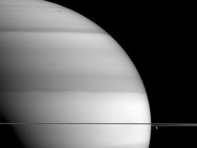 This Sept. 6, 2015 image made available by NASA shows bright-and-dark bands in the atmosphere of Saturn, as seen from the Cassini spacecraft. This image was taken in wavelengths of light that are absorbed by methane. Dark areas are regions where light travels deeper into the atmosphere, passing through more methane. The moon Dione is at right. At bottom are shadows of the planet's rings. (NASA/JPL-Caltech/Space Science Institute via AP)
