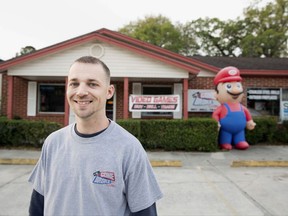 FILE- In this undated file photo provided by the Institute for Justice, Scott Fisher stands outside his video game store in Orange Park, Fla., a suburb of Jacksonville. Attorneys for Gone Broke Gaming have reached an agreement that allows the 9-foot-tall Mario to be out on display once again. Following mediation, the town's attorney sent Fisher a letter on Tuesday, Sept. 26, 2017, saying Orange Park's sign code had been suspended for the store while officials revise the existing rules. (Institute for Justice via AP, File)
