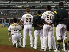 Oakland Athletics' Mark Canha (20) places his hand on the shoulder of Bruce Maxwell as Maxwell kneels during the national anthem for the third consecutive day, prior to the team's baseball game against the Seattle Mariners on Monday, Sept. 25, 2017, in Oakland, Calif. (AP Photo/Ben Margot)