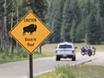 A park ranger and a group of motorcyclists pass a sign warning of bison within the Grand Canyon National Park in northern Arizona.