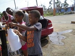 Children fill up bottles with water at a water distribution point, in the aftermath of Hurricane Maria in Loiza, Puerto Rico, Sunday, Sept. 24, 2017. Federal aid is racing to stem a growing humanitarian crisis in towns left without fresh water, fuel, electricity or phone service by the hurricane. (AP Photo/Gerald Herbert)