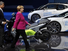 German Chancellor Angela Merkel, right, and the CEO of BMW, Harald Krueger, left, arrive at the booth of the German car manufacturer BMW during Merkel's visit at the Frankfurt Auto Show IAA in Frankfurt, Germany, Thursday, Sept. 14, 2017. (AP Photo/Michael Probst)