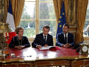 French President Emmanuel Macron, center, signs documents in front of the media to promulgate a new labor bill in his office at the Elysee Palace in Paris, France, as Minister of Labor Muriel Penicaud, left, and Government Spokesman Christophe Castaner look on, Friday, Sept. 22, 2017. Macron has signed Friday five decrees paving the way to the implementation of labor measures aimed at boosting growth, his first major reform since his election. (Philippe Wojazer/Pool Photo via AP)