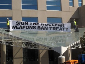 Two anti-nuclear weapons campaigners Gem Romuld, left, and Papatya Danis unfurl a banner at the Department of Foreign Affairs and Trade building in Canberra Wednesday, Sept. 20, 2017, to protest the government's failure to endorse a United Nations' nuclear disarmament treaty. (AP Photo/Rod McGuirk)