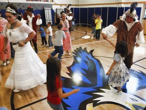 In this Wednesday, Aug. 30, 2017 photo, David Monserat Jaramillo, right, dances with first grade student Harmony Roybal at Tesuque Elementary school in Tesuque, N.M. as Hope Andrea Quintana , left, twirls in white dress. These students and others in Santa Fe's public school district were allowed to skip the annual presentation of Spanish colonial culture and history that honors a 17th century conquistador, in deference to Native American students and others who may find the performances disrespectful. None opted out in Tesuque. Public statues and tributes to early Spanish conquerors are enduring increased criticism tied to the brutal treatment of American Indians centuries ago by soldiers and missionaries. (AP Photo/Morgan Lee)