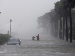 Pedestrians walk by a flooded car on a street as Tropical Storm Irma hits Charleston, S.C., Monday, Sept. 11, 2017. (AP Photo/Mic Smith)