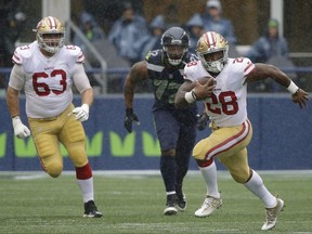 San Francisco 49ers running back Carlos Hyde (28) runs ahead of Seattle Seahawks defensive end Michael Bennett (72) as offensive guard Brandon Fusco (63) looks on in the first half of an NFL football game, Sunday, Sept. 17, 2017, in Seattle. (AP Photo/Elaine Thompson)
