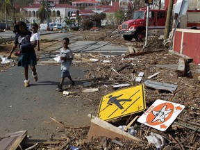 A woman with her two children walk past debris left by Hurricane Irma in Charlotte Amalie, St. Thomas, U.S. Virgin Islands, Sunday, Sept. 10, 2017.  The storm ravaged such lush resort islands as St. Martin, St. Barts, St. Thomas, Barbuda and Anguilla. (AP Photo/Ricardo Arduengo)