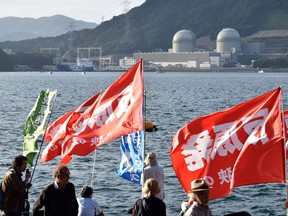 Protesters hold anti-nuclear flags upon the arrival of the Pacific Egret cargo vessel, left in background, carrying MOX, a mixture of plutonium and uranium fuel, at Takahama nuclear power plant in Takahama, western Japan, Thursday, Sept. 21, 2017. A shipload of nuclear fuel containing plutonium returned to Japan after reprocessing in France for use at the Takahama plant as the country tries to burn more plutonium amid international concerns about its stockpile. The plant's operator, Kansai Electric Power Co., said the nuclear fuel is used at its No. 4 reactor, right in background. Second from right in the background is No. 3 reactor. (Madoka Ogawa/Kyodo News via AP)