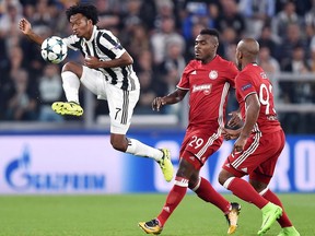 Juventus' Juan Cuadrado, left, goes for the ball ahead of Olympiakos' Emmanuel Emenike and Seb, right, during the Champions League group D soccer match  between Juventus and Olympiakos, at the Allianz stadium in Turin, Italy, Wednesday, Sept. 27, 2017. (Alessandro Di Marco/ANSA via AP)