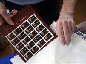 In this May 23, 2017 photo, U.S. Postal Service worker Dianne Zambelli places a sleeve of newly dedicated Henry David Thoreau postage stamps for purchase in a bag at Walden Pond in Concord, Mass. where the 19th century American philosopher and naturalist spent two years in solitude and reflection. The U.S. Postal Service would need to boost prices for mailing letters and packages by nearly 20 percent if it hopes to have enough cash on hand to avoid bankruptcy. That means the price of a first-class stamp could jump from 49 cents to nearly 60 cents, the biggest one-time increase in its history.  (AP Photo/Elise Amendola)